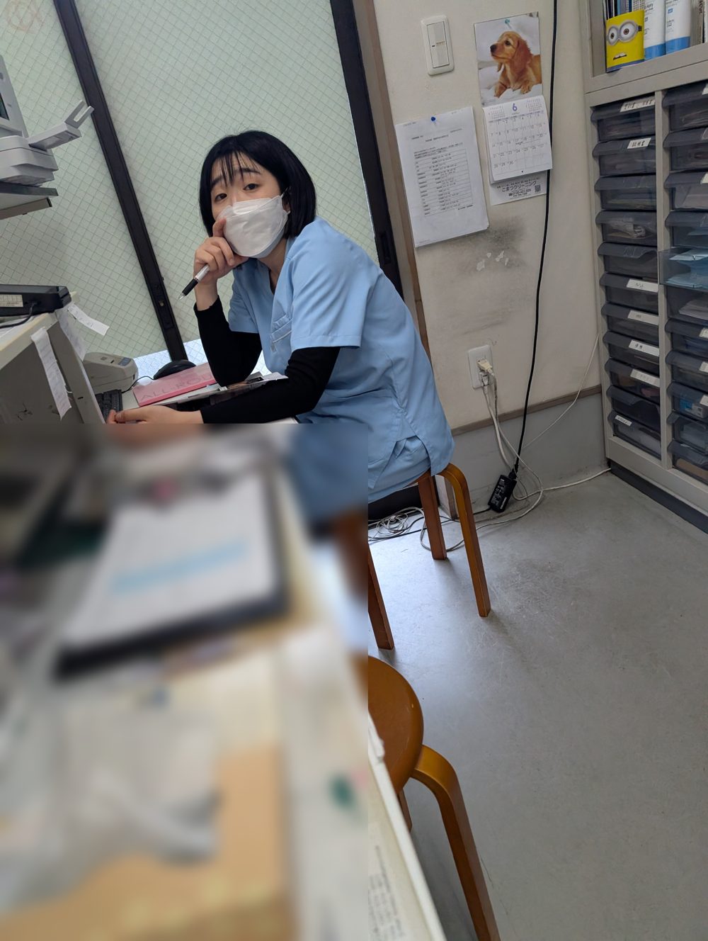 受付の机に座り、こちらを見ている柔道整復師の中尾。マスクを着用。手前の書類はぼかし加工